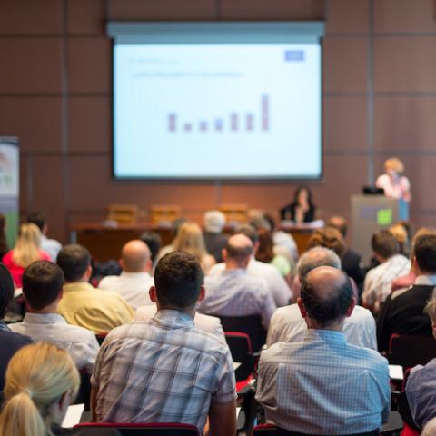 A group of people watching a conference presentation